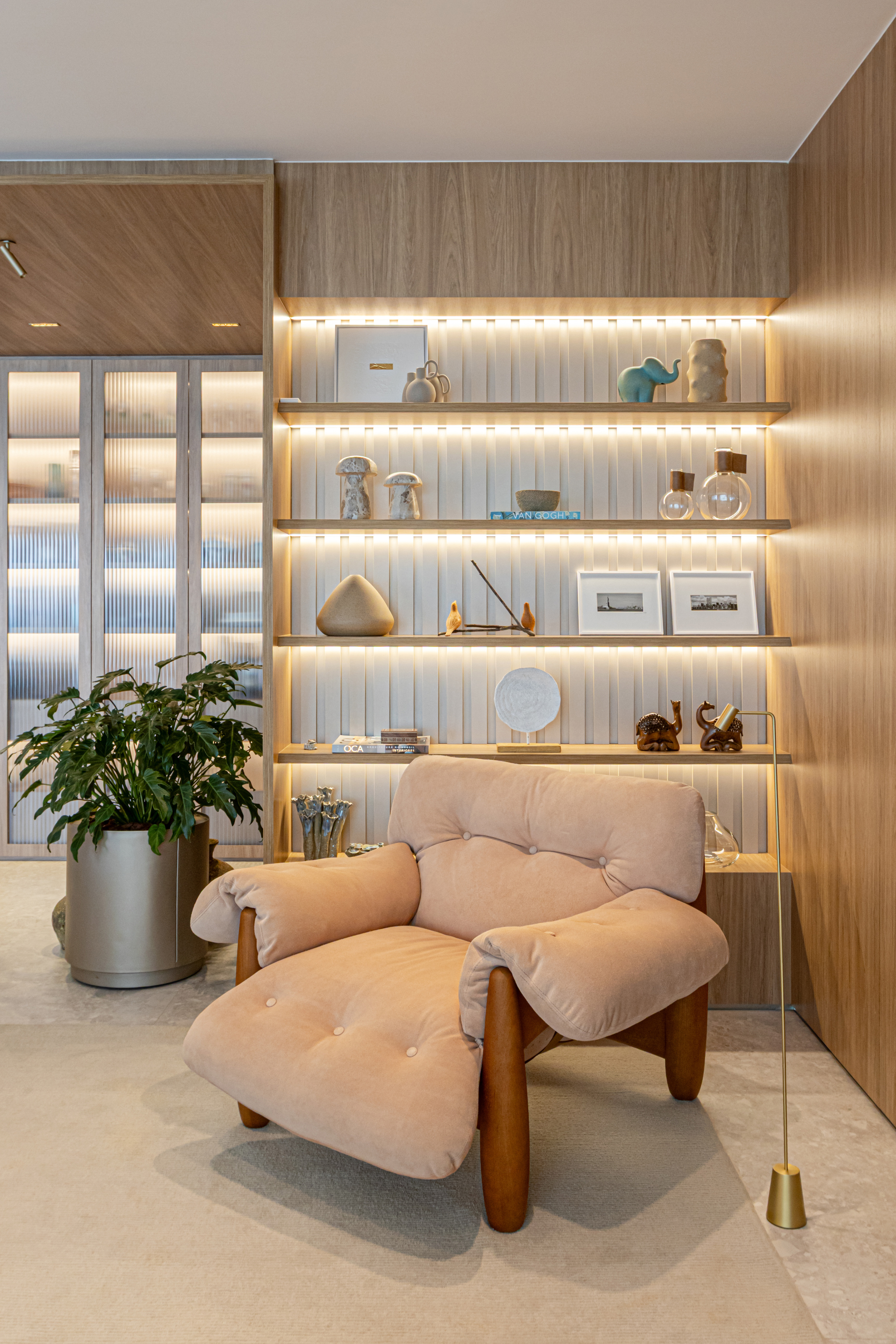 Well-lit living room featuring a luxurious armchair in front of a shelf with decorative objects.